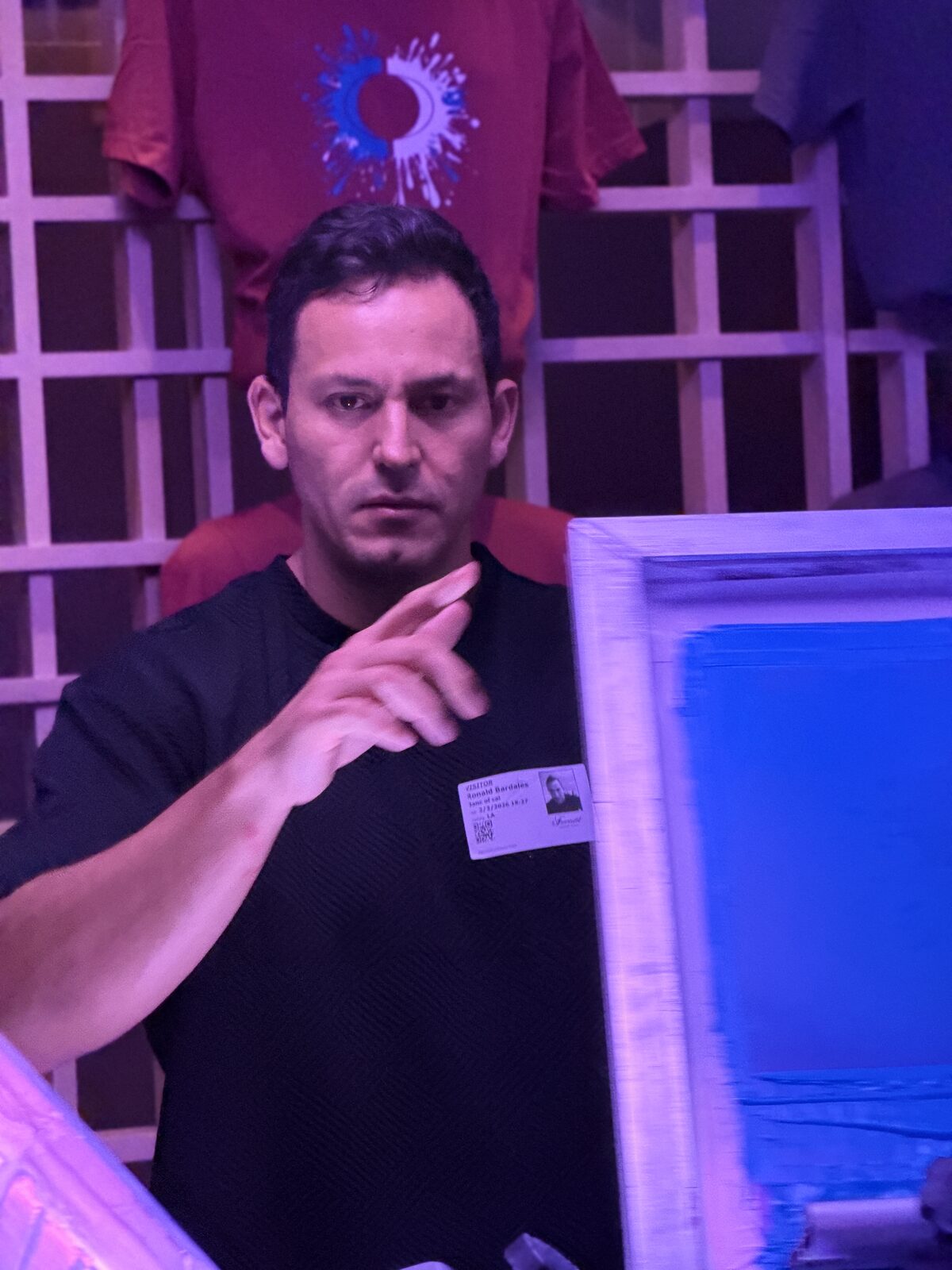 Merch Troop print operator checking a loaded screen at an evening event station with custom shirts displayed behind him